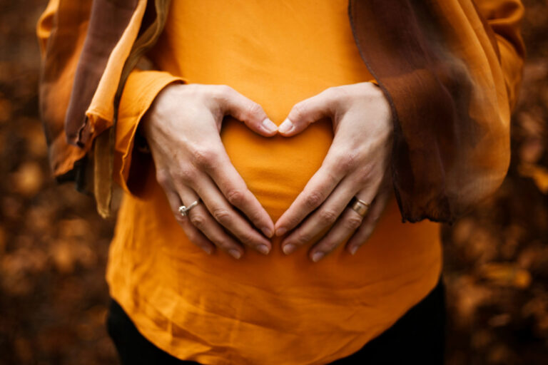 Close up pregnant woman's belly in yellow shirt with hands forming a heart